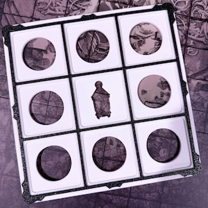 Peut inclure: Un présentoir à neuf compartiments avec un cadre noir et un intérieur blanc. Il contient huit objets circulaires avec un motif et un objet rectangulaire avec une illustration de personnage. Les objets sont dans des tons violets et gris.