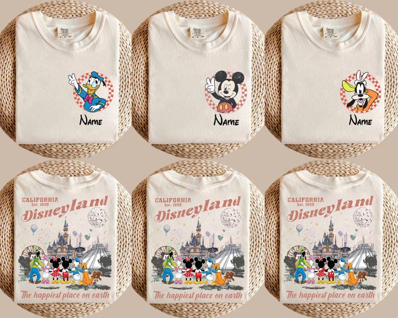 K&ouml;nnte beinhalten: Cremefarbene T-Shirts mit den Disney-Figuren Donald Duck, Mickey Mouse und Goofy, jeweils mit einem Namensfeld. Darunter zeigen drei Shirts eine Disneyland-Grafik mit dem Text "The happiest place on earth."