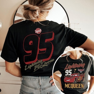 May include: Black t-shirt featuring a large red number 95 with a shadow effect and the words "Lightning McQueen" in a stylized font. The shirt also has the "Rusteze" logo. A smaller image of the shirt is visible in the lower right corner.