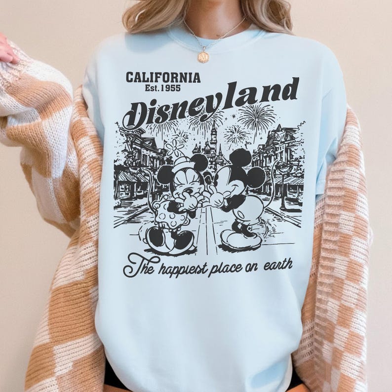 May include: Light blue Disneyland sweatshirt featuring a black and white graphic of Mickey and Minnie Mouse in front of a park scene. The text reads "CALIFORNIA Est.1955 Disneyland" and "The happiest place on earth."