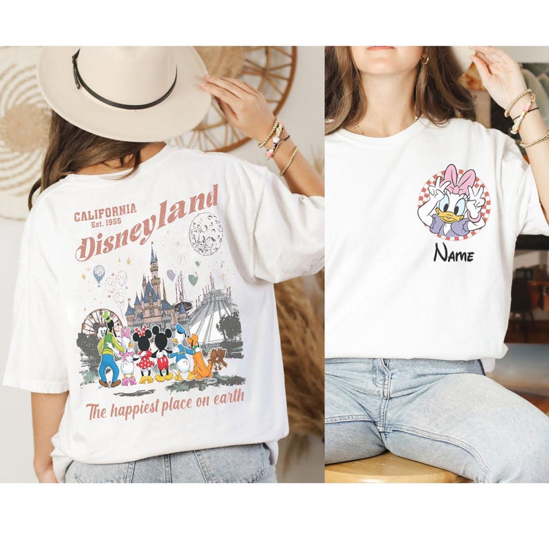 K&ouml;nnte beinhalten: Wei&szlig;e T-Shirts mit Disney-Figuren. Ein Shirt hat eine Disneyland-Grafik auf der R&uuml;ckseite mit dem Text "California Est. 1955" und "The happiest place on earth". Das andere Shirt hat eine Daisy Duck-Grafik mit dem Text "Name".