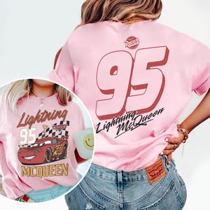 May include: Pink t-shirt featuring a graphic of Lightning McQueen from the Cars movie. The front of the shirt displays the text "Lightning 95 McQueen" with an image of the car. The back of the shirt has a large "95" and "Lightning McQueen" text.