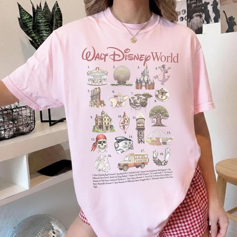 K&ouml;nnte beinhalten: Hellrosa T-Shirt mit dem Schriftzug "Walt Disney World". Das Shirt zeigt Illustrationen von Disney-Parkattraktionen, wie ein Karussell, Spaceship Earth und Cinderella Castle, mit einer Liste von Attraktionen darunter.