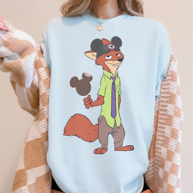 Puede incluir: Sudadera azul claro con un personaje de zorro de dibujos animados que lleva un sombrero de Mickey Mouse y sostiene un helado con forma de Mickey Mouse. El zorro viste una camisa verde, una corbata morada y pantalones marrones.