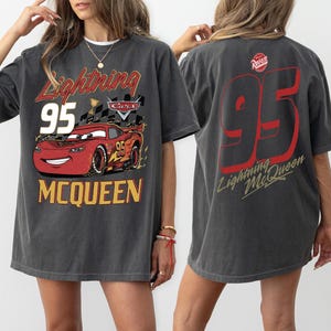 May include: Dark gray t-shirt featuring Lightning McQueen from the Cars movie. The front graphic includes the text "Lightning 95 McQueen" with a red race car. The back of the shirt displays a large "95" and "Lightning McQueen" in red.
