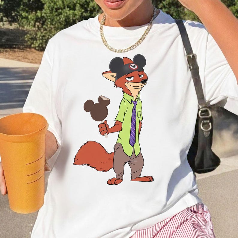 Puede incluir: Camiseta blanca con un personaje de zorro de dibujos animados que lleva un sombrero con orejas de Mickey Mouse, una camisa verde y una corbata morada. El zorro sostiene un helado de chocolate. La camiseta es una prenda informal.