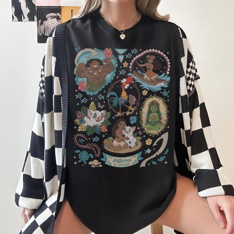 May include: Black graphic tee featuring characters from the animated film Moana, including Maui, Moana, Pua, Hei Hei, and others. The tee is paired with a black and white checkered cardigan.