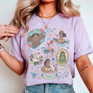 May include: A light purple t-shirt featuring illustrations of characters from the animated film Moana. The design includes images of Maui, Moana, Hei Hei, Pua, and others, with the words "Moana & Friends" at the bottom.