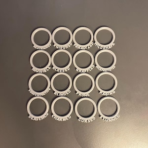 May include: A set of 16 gray plastic rings with different words printed on them. The words are: Restrained, Poisoned, Paralyzed, Wildshape, Invisible, Blessed, Grappled, Incapacitated, Concentrating, Blinded, Prone, Raging, Deafen, Charmed, Cursed, Stunned.