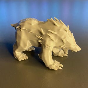 Puede incluir: Una figurita de oso gris impresa en 3D con una superficie texturizada y una expresión feroz.