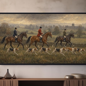 May include: A framed landscape painting depicting three riders on horseback wearing formal equestrian attire, accompanied by a pack of running hounds in a grassy field. The background features a cloudy sky, rolling hills, and a distant stone building.