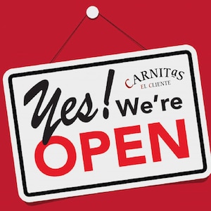 May include: A white sign with black trim hangs from a red wall. The sign says "Yes! We're OPEN" in black and red lettering. The top of the sign has a logo that says "Carnitas El Cliente" in red and black lettering.