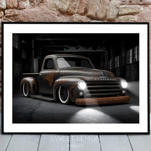 Könnte beinhalten: Ein alter, rostiger, dunkelgrauer Pick-up mit dem Schriftzug "Studebaker" auf dem Kühlergrill. Der Wagen steht in einer dunklen, industriellen Umgebung, beleuchtet von Scheinwerfern.
