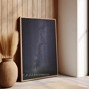 May include: A framed print of a black and white photograph of the Milky Way galaxy over a long, narrow bridge with lights. The bridge is silhouetted against the night sky.