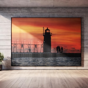 May include: A framed landscape art print featuring a lighthouse silhouetted against a vibrant sunset. The artwork depicts a pier with figures, set against a fiery orange and red sky. The print is displayed in a modern interior setting.