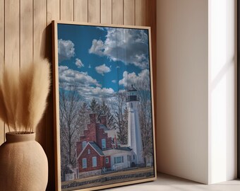 May include: A framed wall art print featuring a tall white lighthouse next to a red brick building with a stepped gable roof. The scene is set against a bright blue sky with scattered white clouds and bare trees in the background.