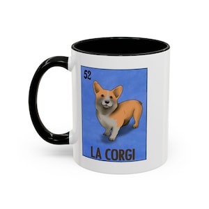 Könnte beinhalten: Weißer Keramikbecher mit schwarzem Griff und Innenraum. Der Becher zeigt ein blaues Rechteck mit einer Cartoon-Corgi-Hundeillustration und dem Text "LA CORGI". Die Nummer "52" befindet sich in der oberen linken Ecke.
