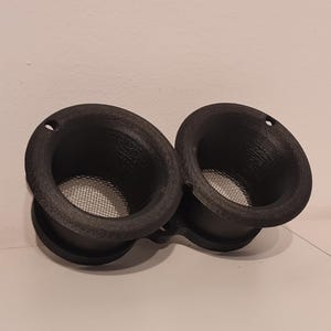 Op de afbeelding: Twee zwarte plastic luchtinlaten met gaas. De trechters zijn aan elkaar verbonden.
