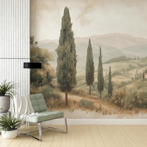 May include: A watercolour painting of a Tuscan landscape with rolling hills, green trees, and a small house in the distance. The painting is framed and hanging on a white wall.