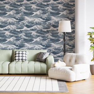 Puede incluir: Un diseño de interior de sala de estar con un sofá verde claro, un sillón blanco y una lámpara de pie. La pared está cubierta con un papel tapiz azul y blanco con un patrón repetitivo de olas estilizadas.
