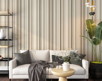 May include: A white sofa with gray throw pillows and a gray blanket sits in front of a wall with vertical stripes in beige and brown. A small wooden table with a white vase of flowers sits in front of the sofa. A potted plant with large green leaves is in the corner of the room.