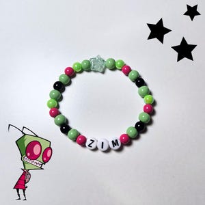 Può includere: Un braccialetto di perline con il nome "ZIM" scritto con perline di lettere bianche. Il braccialetto presenta perline verdi, rosa e nere, con una perlina trasparente a forma di stella al centro. Sono presenti anche un personaggio dei cartoni animati e forme di stelle nere.