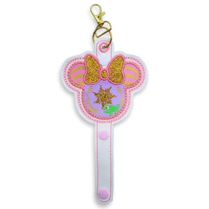 May include: White and pink key fob with a gold-coloured clasp. The key fob features a Minnie Mouse head design with a gold glitter bow, a purple centre with a sun emblem, and a green chameleon.