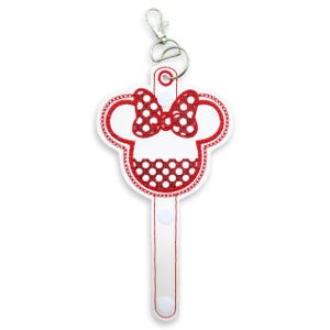 May include: A white and red embroidered keychain with a Minnie Mouse design. The keychain features a red polka dot bow and a red outline. It includes a silver metal clasp for attachment.