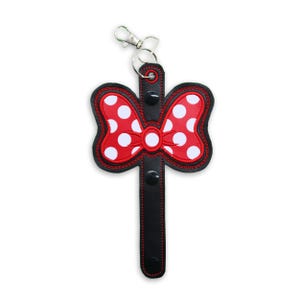May include: A red and white polka dot bow with a black strap and a silver key ring. The bow is attached to a black strap with a silver key ring.