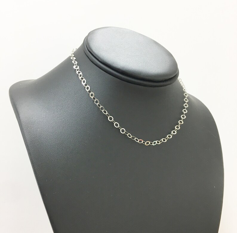 Puede incluir: Un collar de cadena de plata en un expositor negro. La cadena est&aacute; hecha de peque&ntilde;os eslabones redondos.