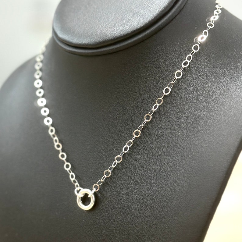 Puede incluir: Un collar de cadena de plata con un peque&ntilde;o colgante circular.