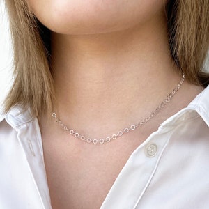 Puede incluir: Un collar de cadena de plata con un delicado dise&ntilde;o de eslabones circulares. El collar lo lleva una persona con el pelo casta&ntilde;o claro y una camisa blanca.