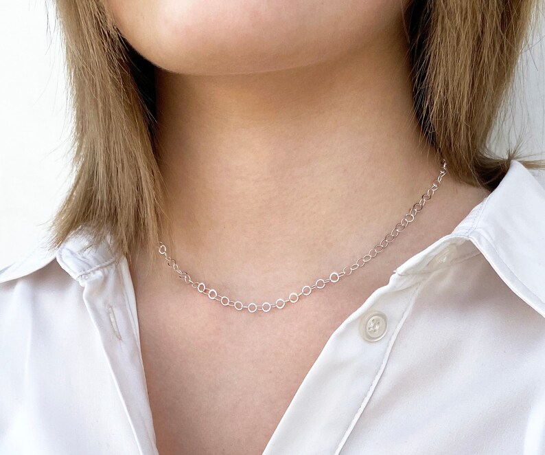 Puede incluir: Un collar de cadena de plata con un delicado dise&ntilde;o de eslabones circulares. El collar lo lleva una persona con el pelo casta&ntilde;o claro y una camisa blanca.