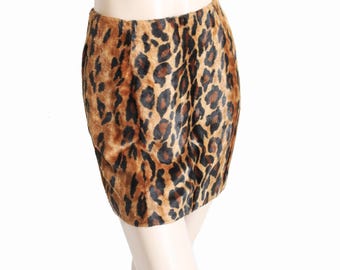 May include: A mini skirt with a leopard print pattern. The skirt features a brown and black spotted design on a tan background. The skirt is made of a soft, textured material.