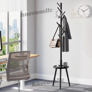 May include: A black coat rack with a shelf and multiple hooks. The rack has a tree branch design and is standing on a gray carpet. The rack is in a room with a window and a desk with a chair.