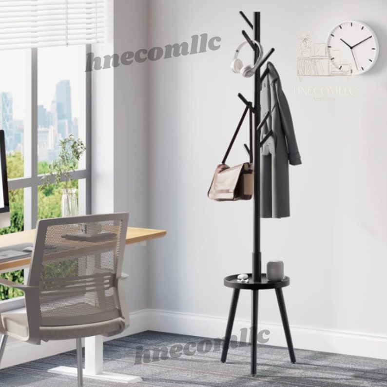 May include: A black coat rack with a shelf and multiple hooks. The rack has a tree branch design and is standing on a gray carpet. The rack is in a room with a window and a desk with a chair.