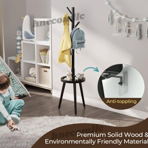 May include: Black wooden coat rack with a shelf and four hooks. The rack has a round shelf and three legs. The rack is in a room with a white bookcase and a rug. The text "Anti-toppling" is visible in the image.