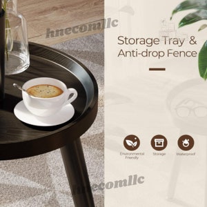 May include: A black round side table with a storage tray and an anti-drop fence. The table has three black legs and a cup of coffee on the tray. The text "Storage Tray & Anti-drop Fence" is written in brown text on a white background. The text "Environmental Friendly", "Storage", and "Waterproof" is written in black text on white circles with icons.