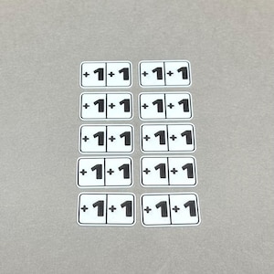 Puede incluir: Diez azulejos rectangulares blancos con bordes negros y el texto "1 + 1" impreso en cada azulejo.