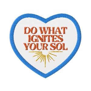 May include: Embroidered heart-shaped patch with a blue border and white center. The patch features the text "DO WHAT IGNITES YOUR SOL" in orange, with a yellow sun design at the bottom. This patch is suitable for jackets, bags, or other fabric items.