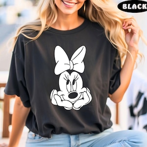May include: Black t-shirt with a white graphic of Minnie Mouse with a bow. Minnie Mouse is smiling and has her hands clasped in front of her.
