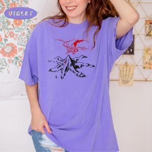May include: A purple t-shirt with a black and red graphic of a dragon flying over a mountain.