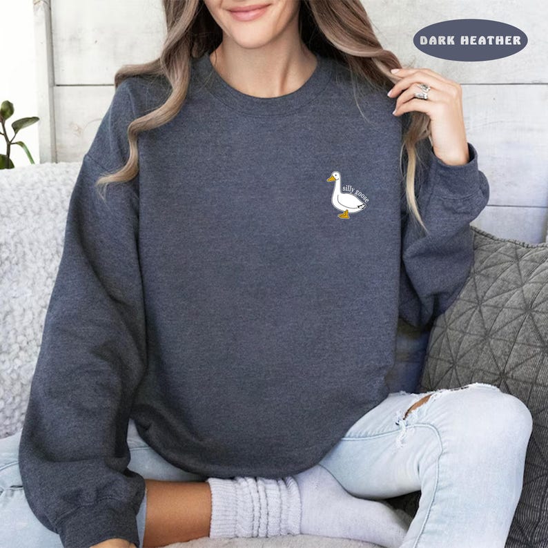 May include: A dark heather grey sweatshirt with a white goose graphic and the text "silly goose" on the front.