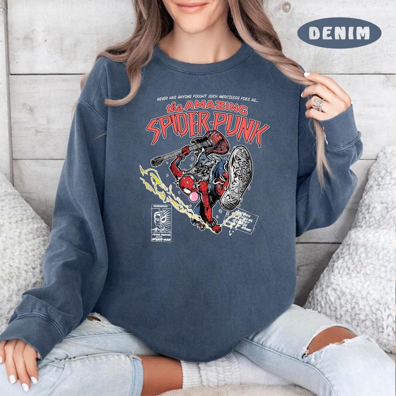 Puede incluir: Una sudadera azul con un gr&aacute;fico de un personaje de Spider-Man rojo y negro tocando una guitarra. El texto "The Amazing Spider-Punk" est&aacute; impreso en la sudadera.
