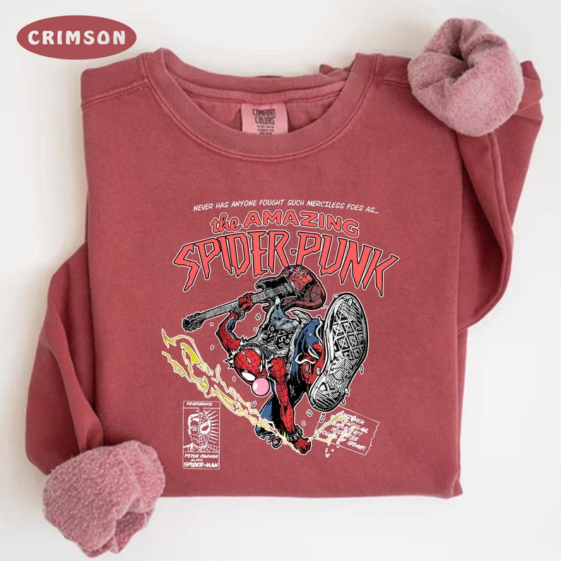 Puede incluir: Una sudadera roja de manga larga con un estampado gr&aacute;fico de un superh&eacute;roe de dibujos animados tocando la guitarra. El texto en el gr&aacute;fico dice "NEVER HAS ANYONE FOUGHT SUCH MERCILESS FOES AS... the AMAZING SPIDER-PUNK".