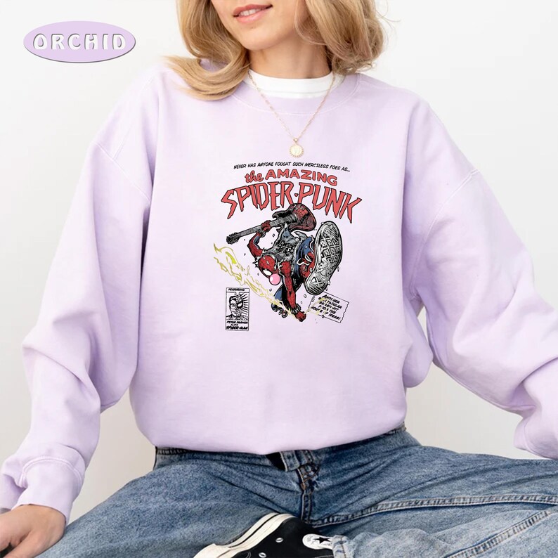 Puede incluir: Una sudadera de color lavanda con un estampado gr&aacute;fico de un superh&eacute;roe de dibujos animados tocando la guitarra. El texto en el gr&aacute;fico dice "The Amazing Spider-Punk".