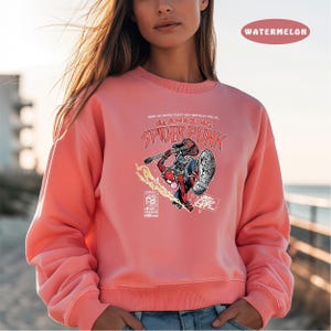 Puede incluir: Una sudadera rosa con un gr&aacute;fico de Spider-Man tocando la guitarra. El texto "The Amazing Spider-Punk" est&aacute; impreso en la sudadera.