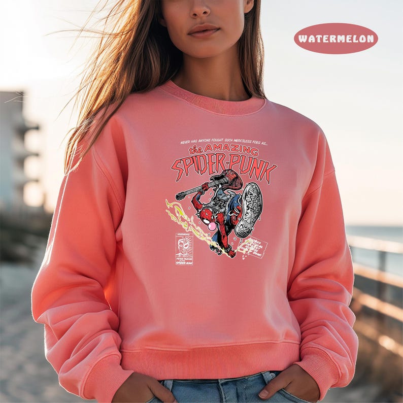 Puede incluir: Una sudadera rosa con un gr&aacute;fico de Spider-Man tocando la guitarra. El texto "The Amazing Spider-Punk" est&aacute; impreso en la sudadera.