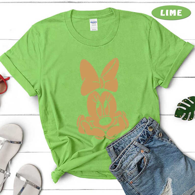 May include: A lime green t-shirt with a cartoon image of a mouse with large ears and a bow. The mouse is in a sitting position with its hands on its lap. The text "LIME" is in the upper right corner of the image.