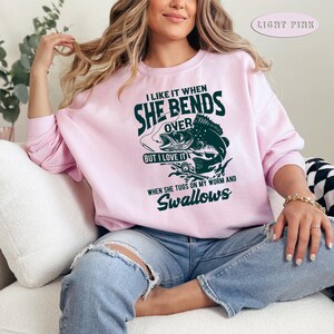May include: Light pink sweatshirt with a fishing-themed graphic that says "I like it when she bends over but I love it when she tugs on my worm and swallows".